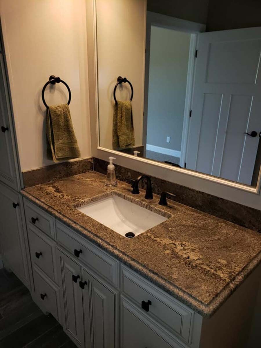 Bathroom vanity with white cabinets, granite countertop, mirror, and towel ring.