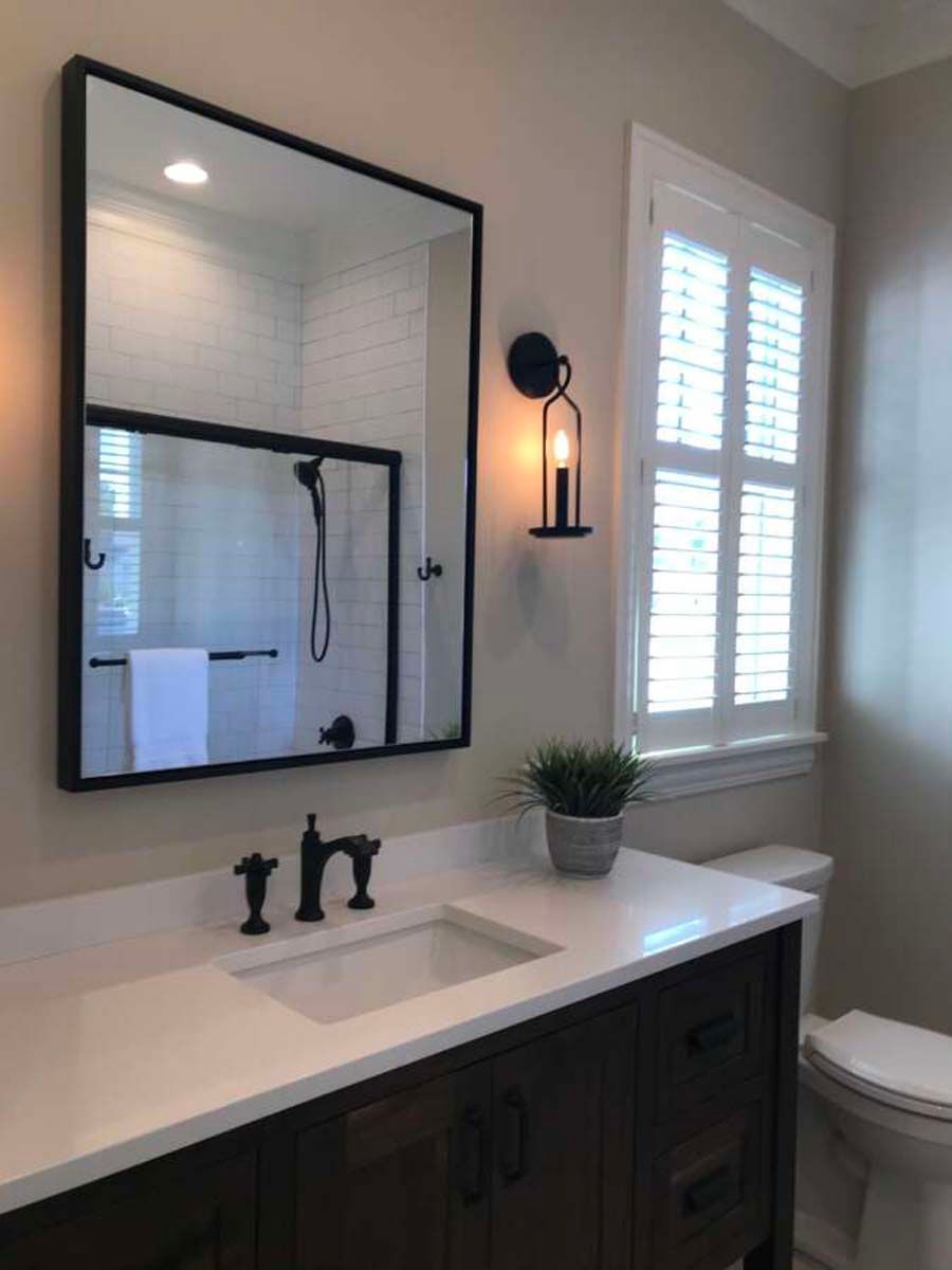 Bathroom with dark wood vanity, white countertop, black mirror, and a window with white shutters.