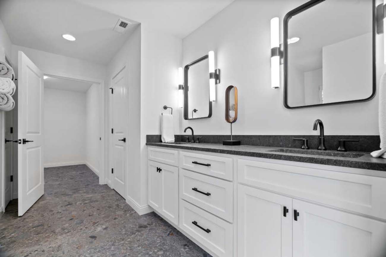 Modern bathroom with white cabinets, black countertops, and two mirrors with sconces.