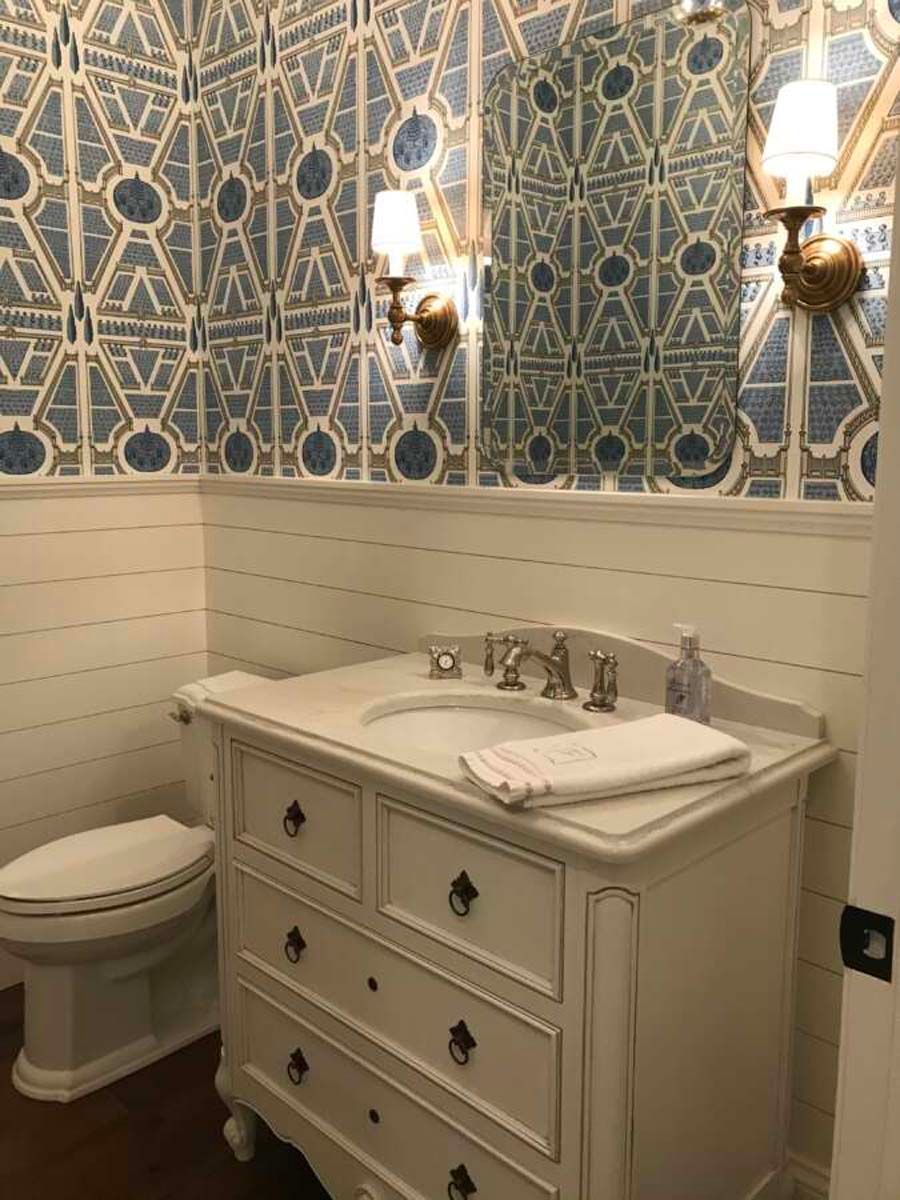 Powder room with blue and white patterned wallpaper, white vanity, sconces, and toilet.