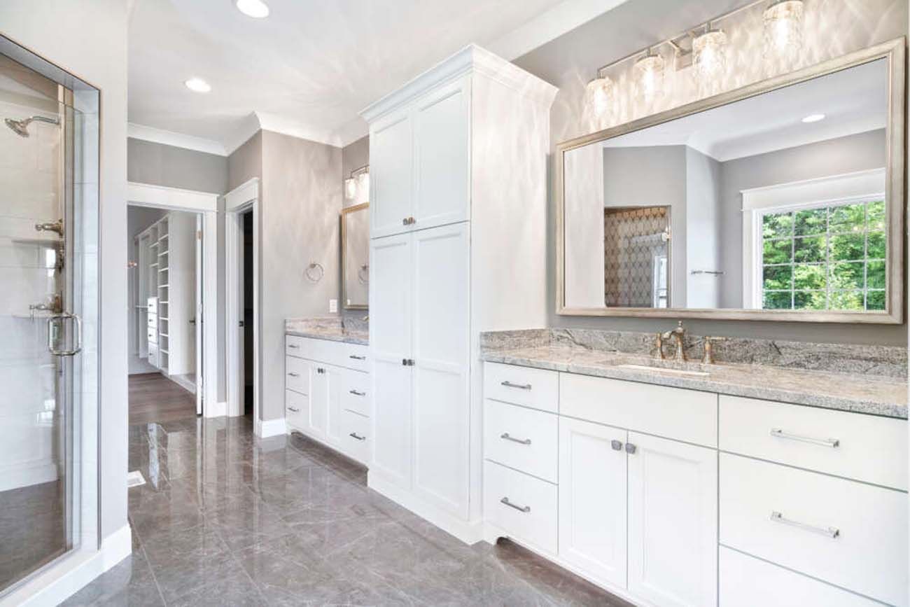 Spacious white bathroom with gray floor and countertops, double vanity, tall storage cabinet, and large mirror.
