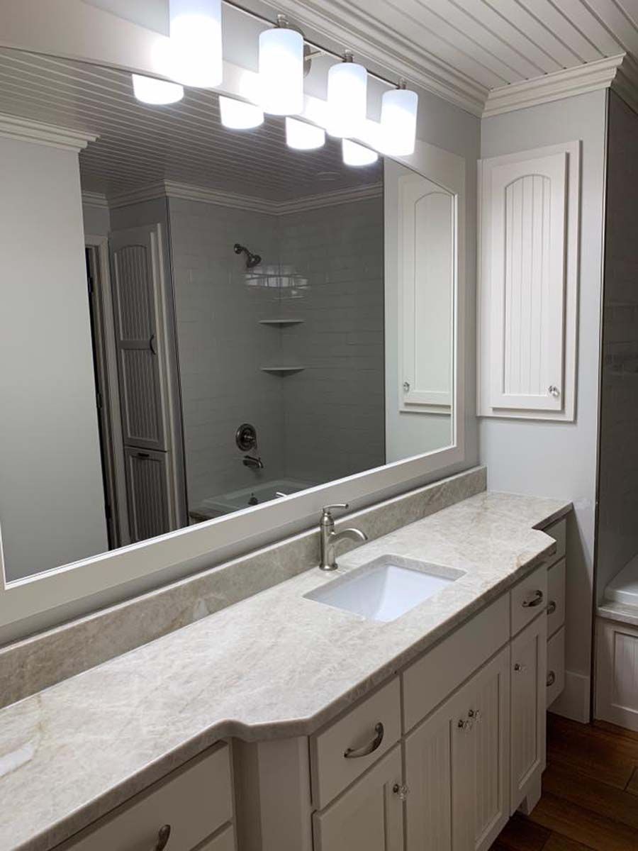 Bathroom with white cabinets, light countertop, large mirror, and overhead lights.