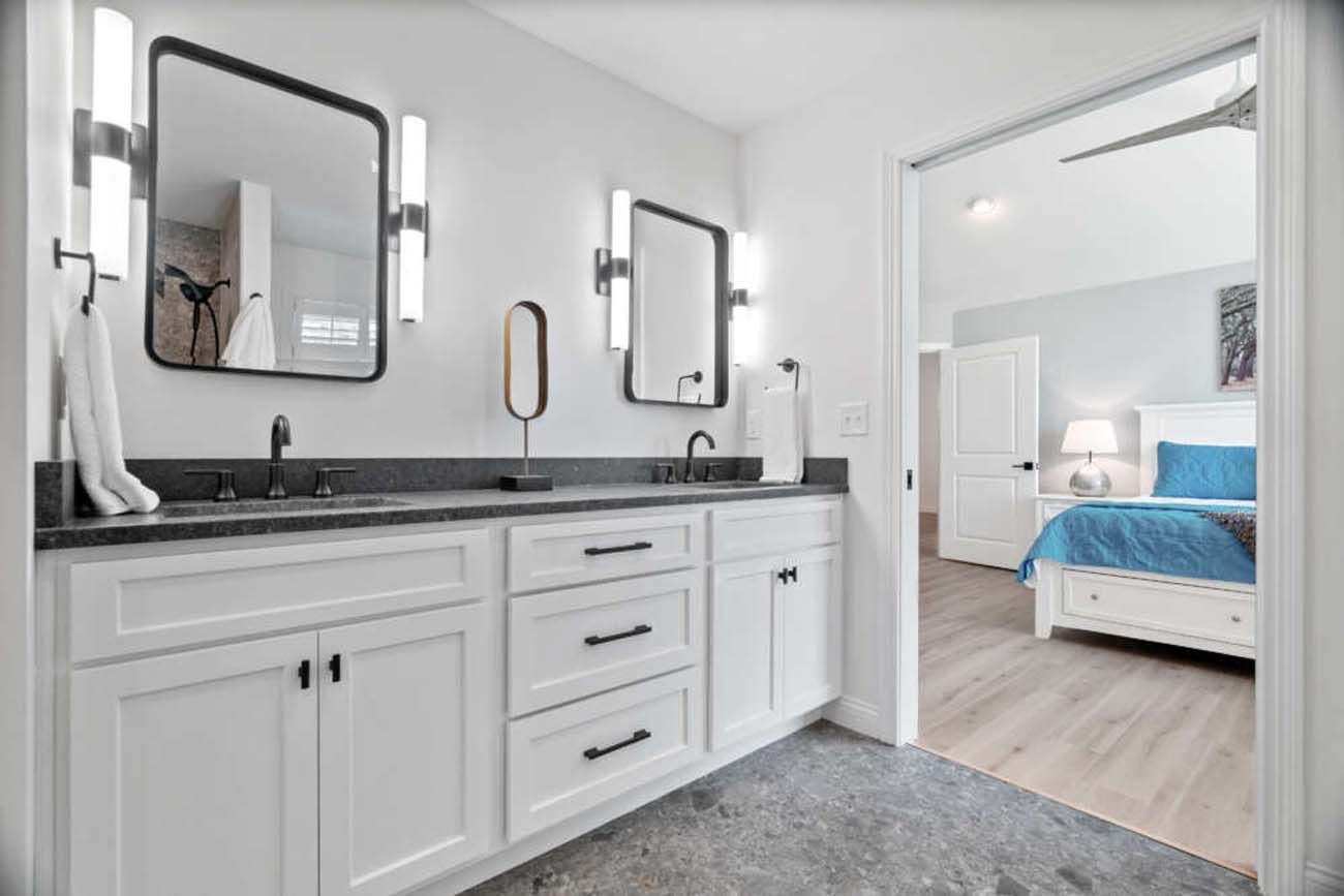 Modern white bathroom with double vanity, black mirrors, and a view into the bedroom.