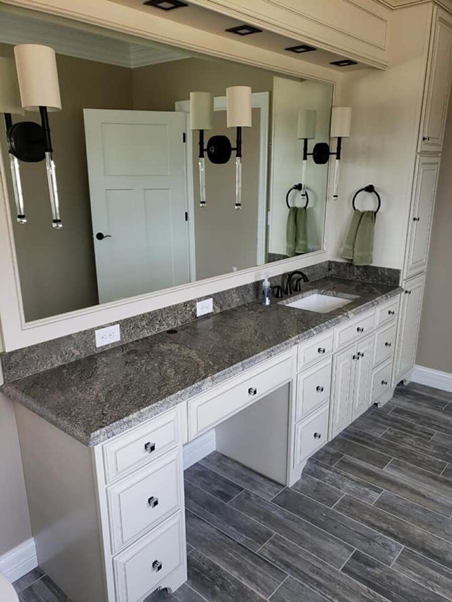 Bathroom vanity with a gray countertop, white cabinets, and a large mirror. Two sconces and a towel rack are visible.