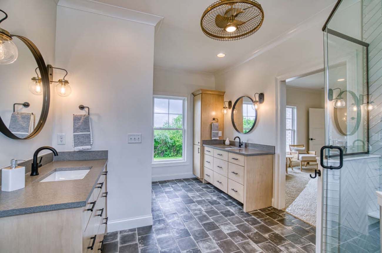 Bathroom with two vanities, round mirrors, and glass shower. Dark tiled floor, white walls.