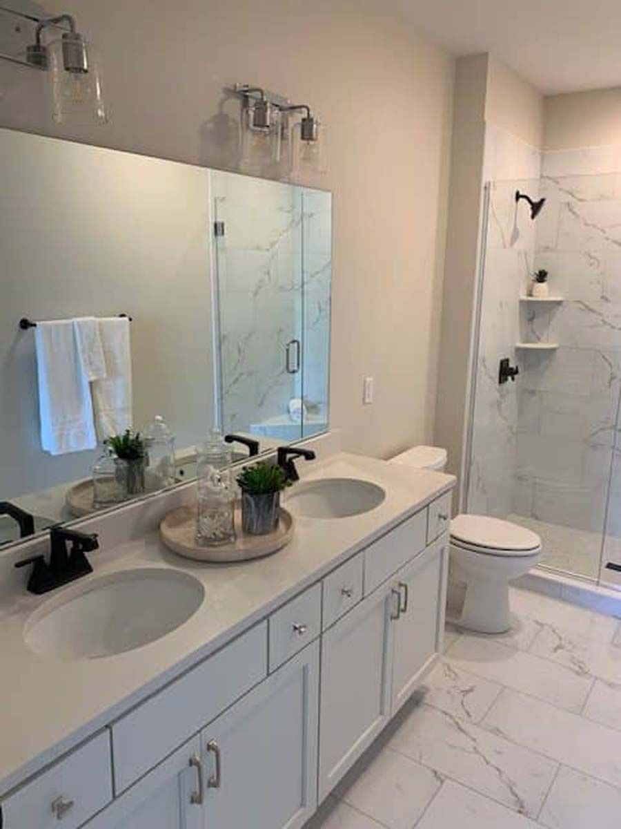White bathroom with dual sinks, marble accents, and a glass-enclosed shower.