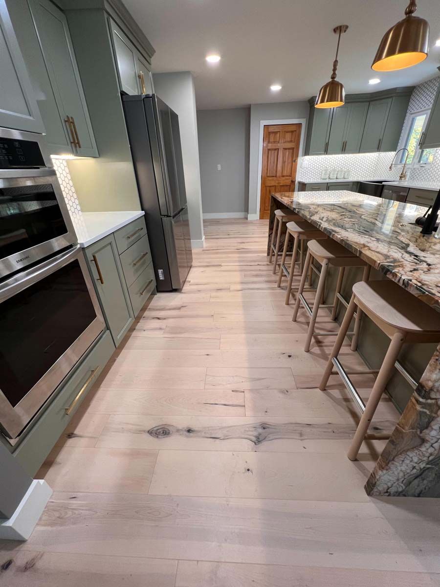 Kitchen with light wood floor, green cabinets, stainless steel appliances, and a granite island with stools.