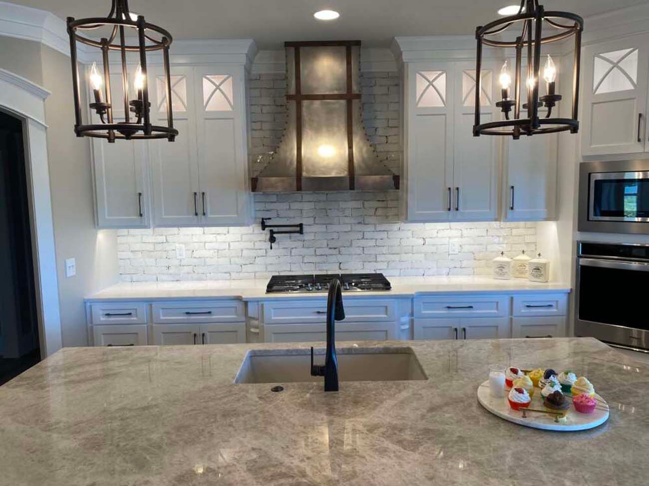 Elegant white kitchen with granite countertops, stainless steel appliances, and two hanging black light fixtures.