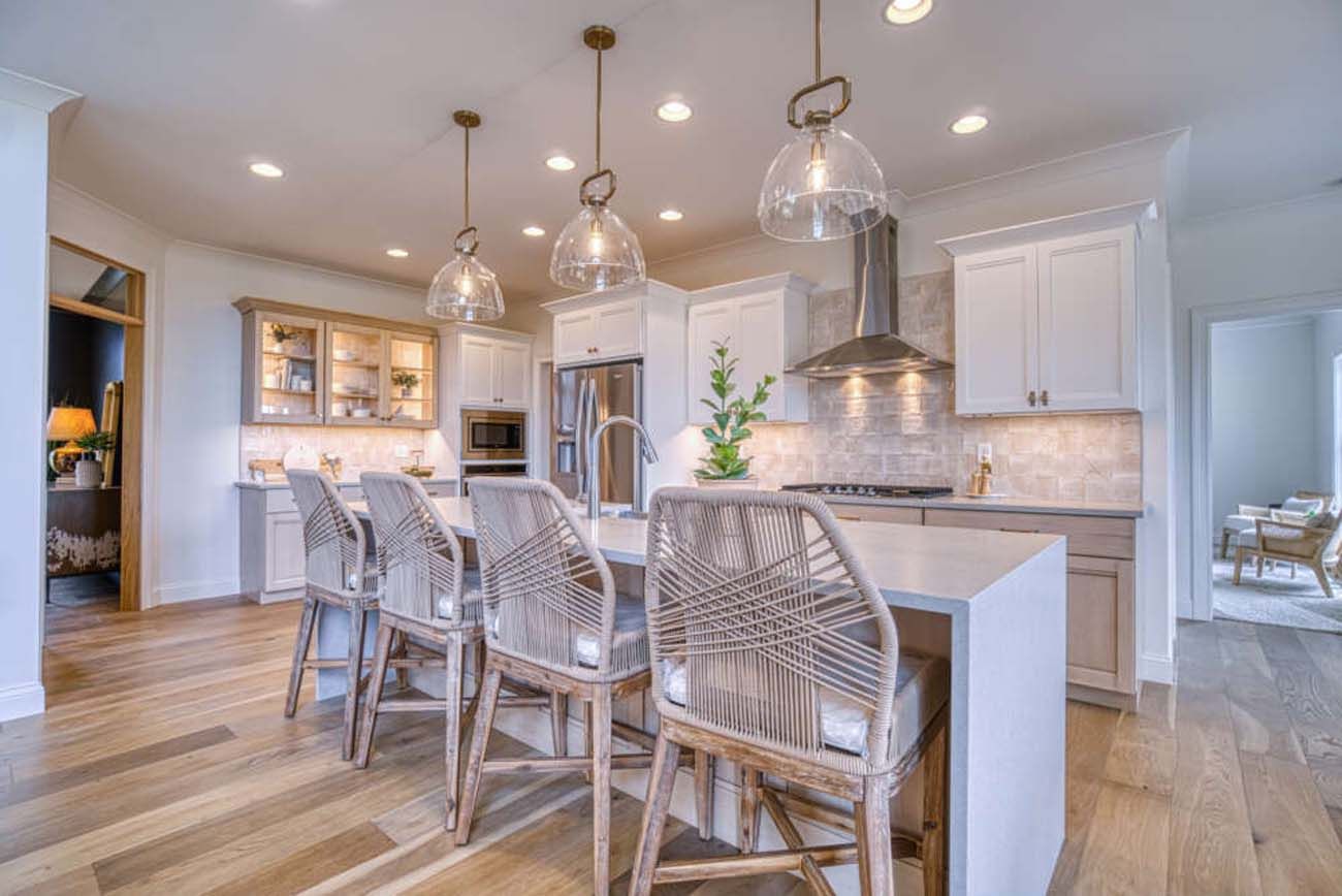 Modern kitchen with island, pendant lights, stainless steel appliances, and wooden flooring.