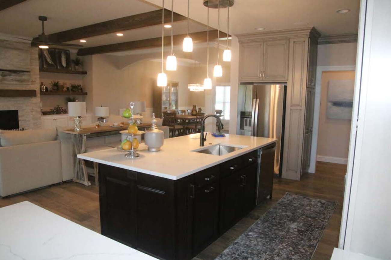 Kitchen with dark island, white countertops, hanging lights, light cabinets, and open to living space.