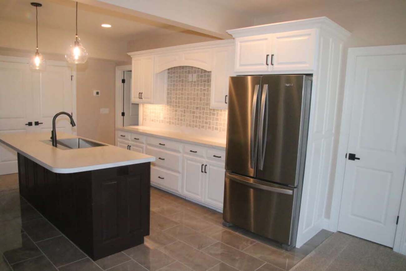 Modern kitchen with white cabinets, dark island, and stainless steel refrigerator.