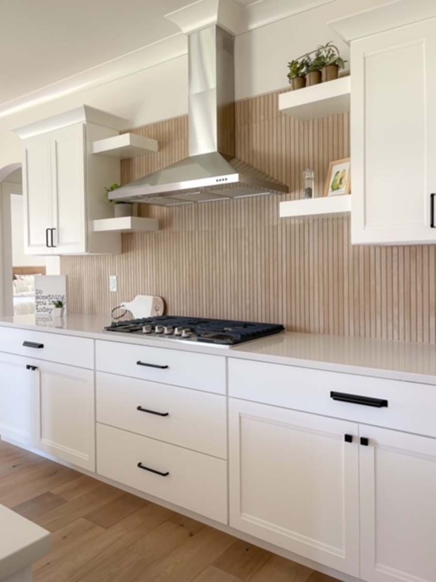 White kitchen with light wood backsplash, stainless steel hood, and black hardware.