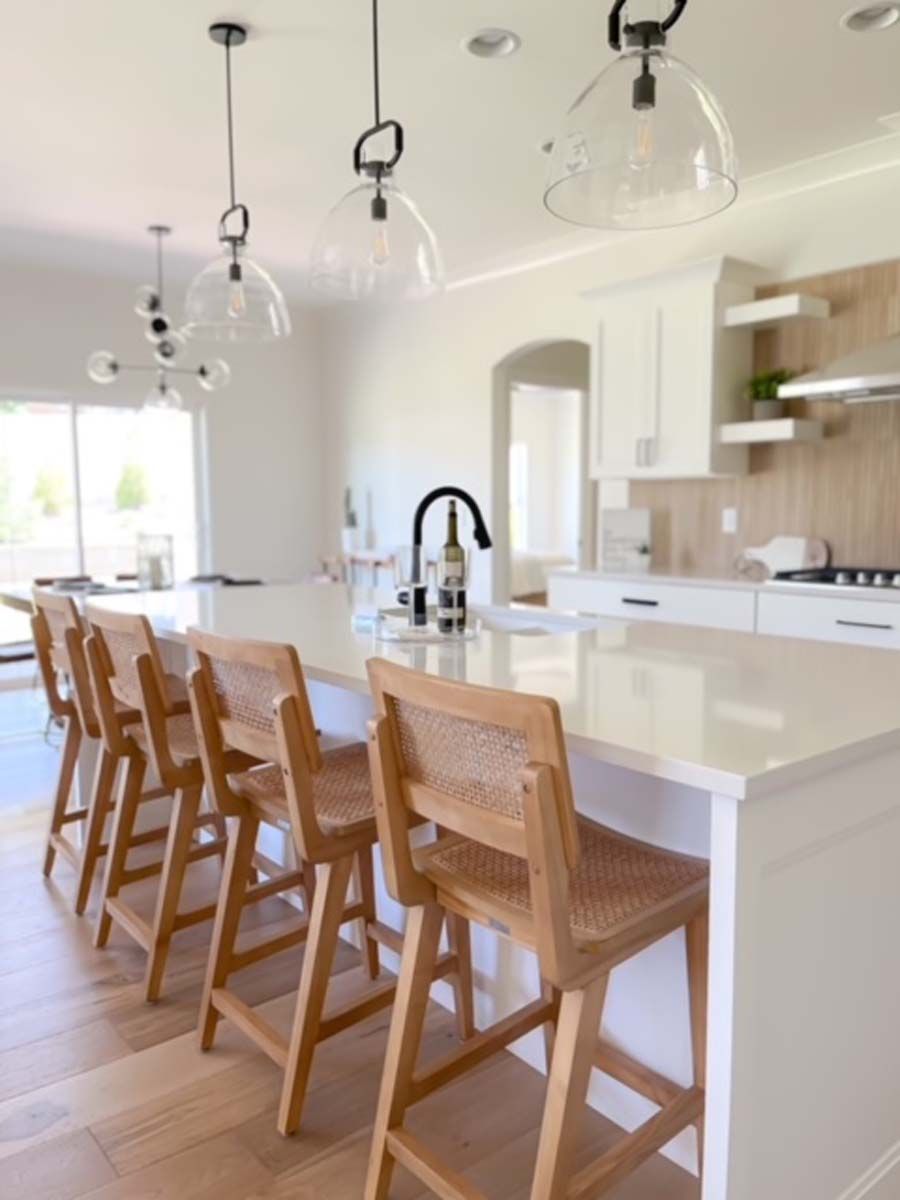 Kitchen with white cabinets, island, and wooden stools. Clear pendant lights hang above.