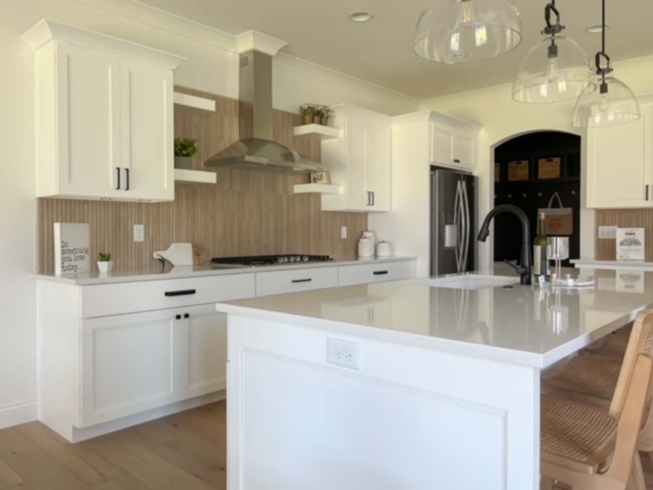 White kitchen with wood backsplash and island, stainless steel appliances, and clear glass pendant lights.
