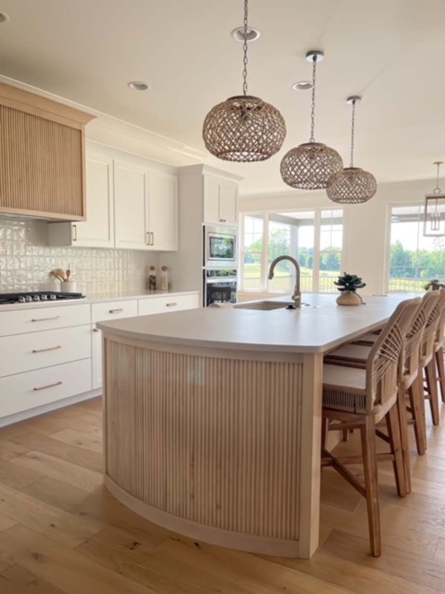 Modern kitchen with white cabinets, wood accents, and a curved island with pendant lights.