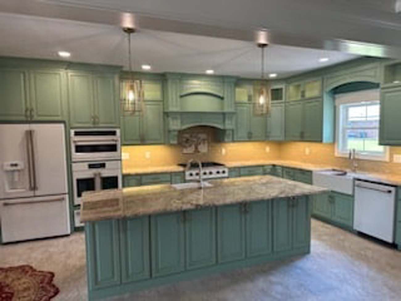 Green kitchen with island, white appliances, and granite countertops.