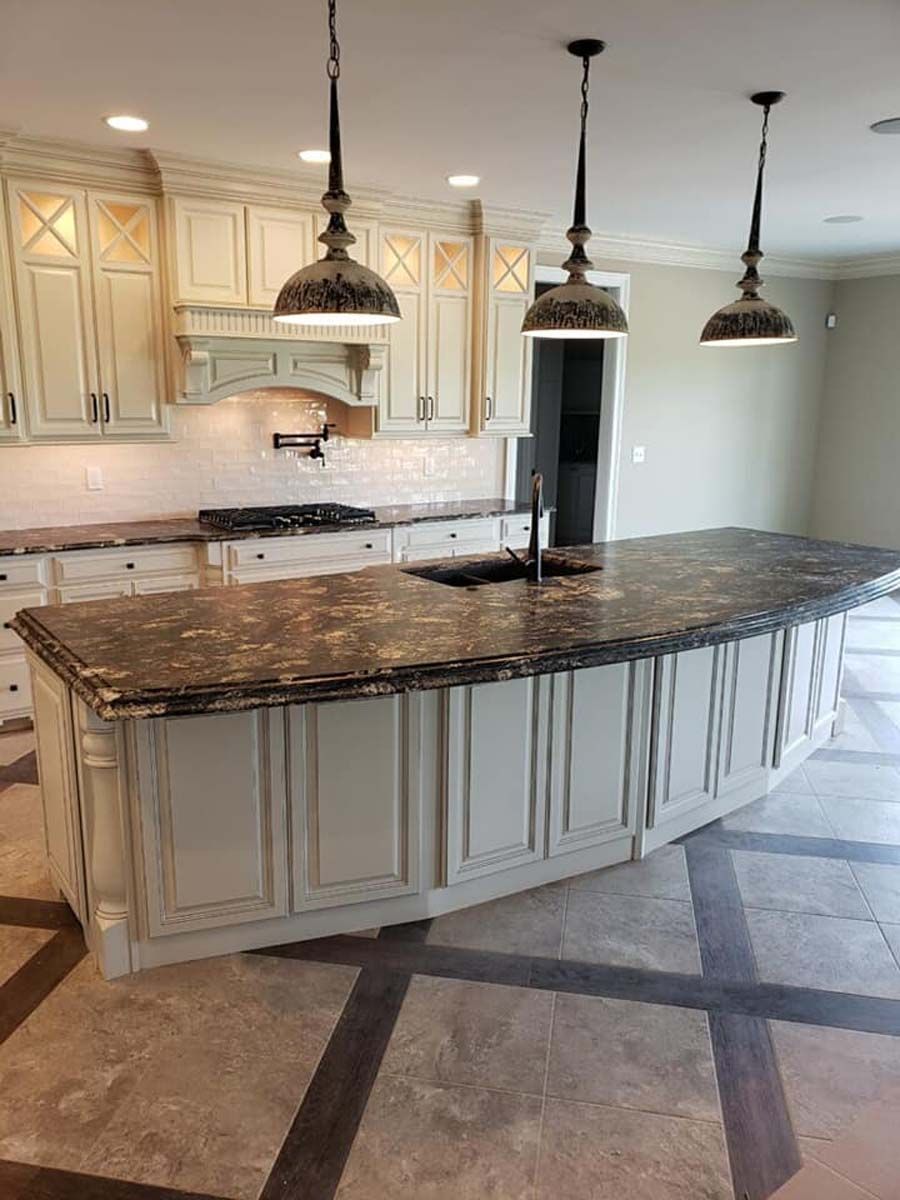 Kitchen with cream cabinets, dark countertop island, pendant lights.