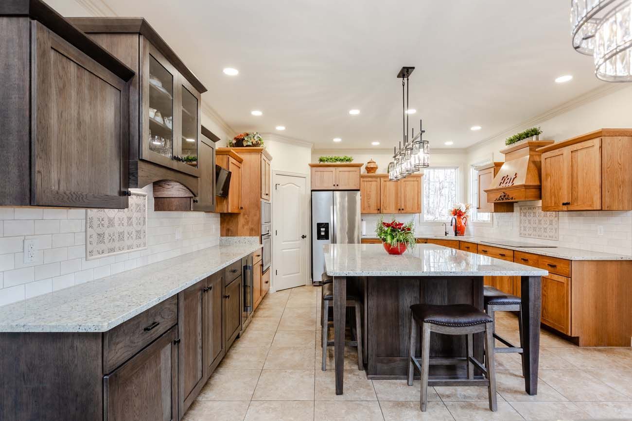 Modern kitchen with gray and wood cabinets, white countertops, and an island with stools.