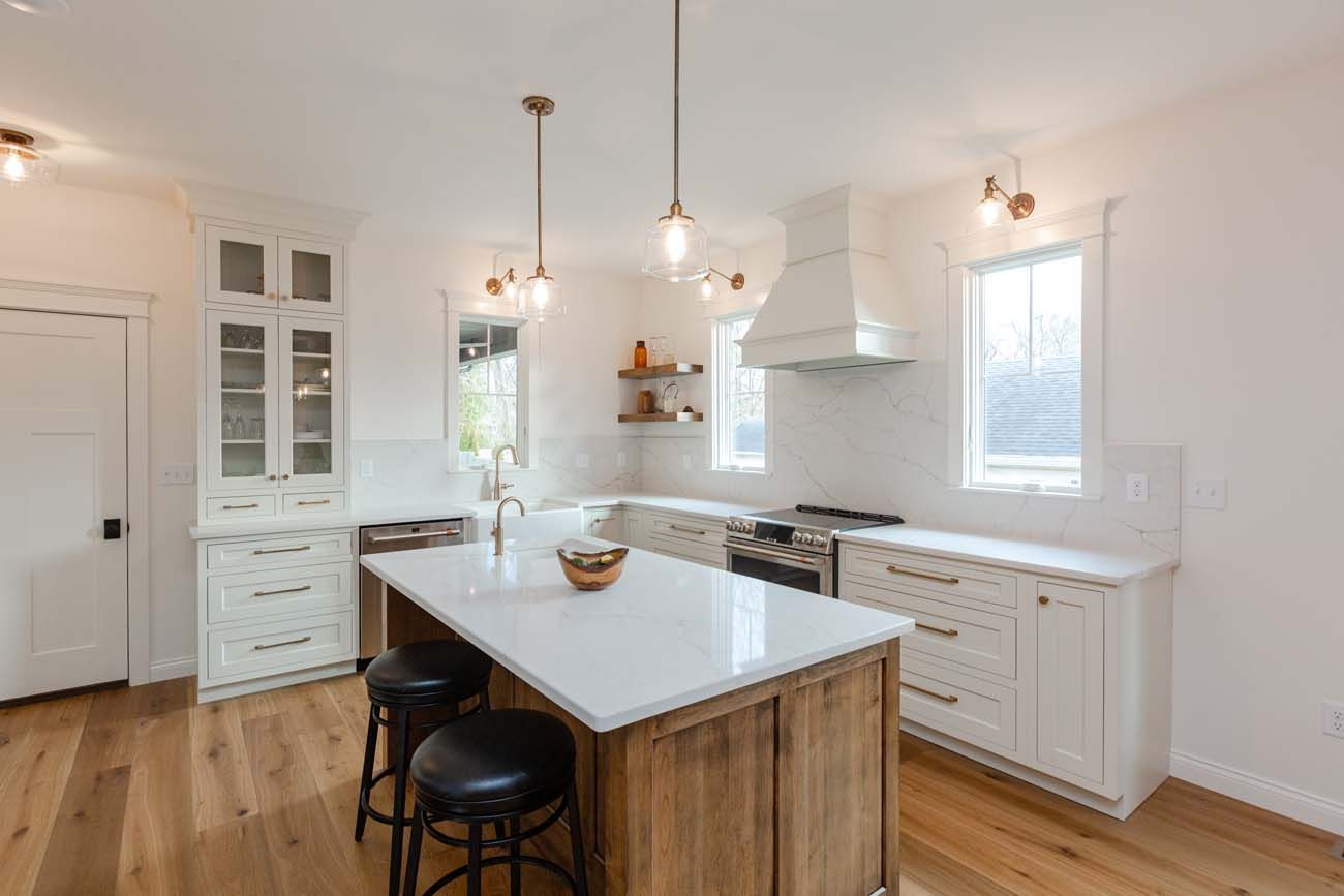 Modern kitchen with white cabinets, island, wooden floor, and pendant lights.