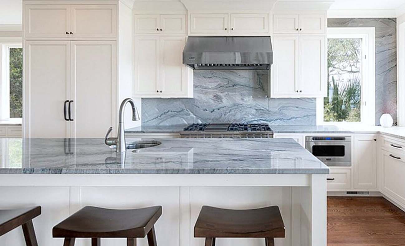 White kitchen with gray countertop and backsplash, stainless steel appliances, and wooden stools.