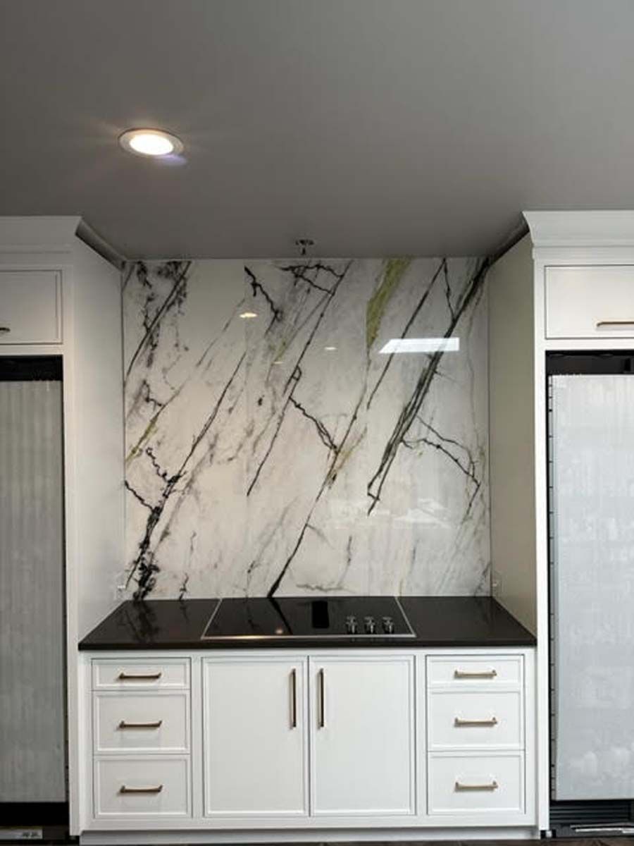 White kitchen cabinets with black countertop and marble backsplash.
