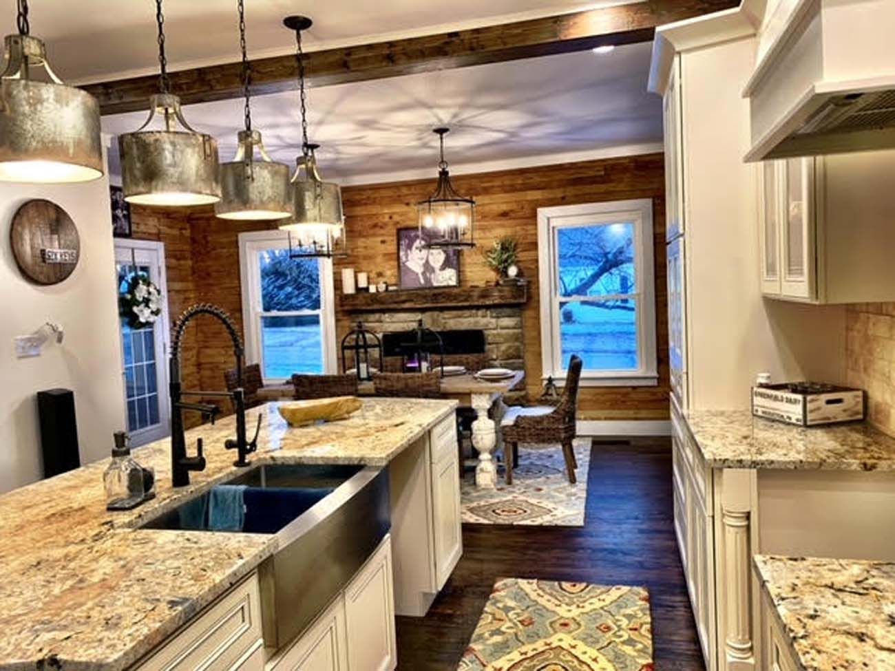 Kitchen with granite countertops, wood accents, and stainless steel sink, overlooking a dining area with a fireplace.