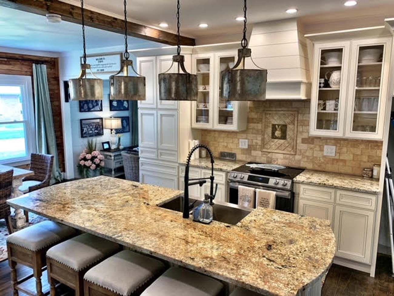 Kitchen with granite countertop island, white cabinets, and metal pendant lights.