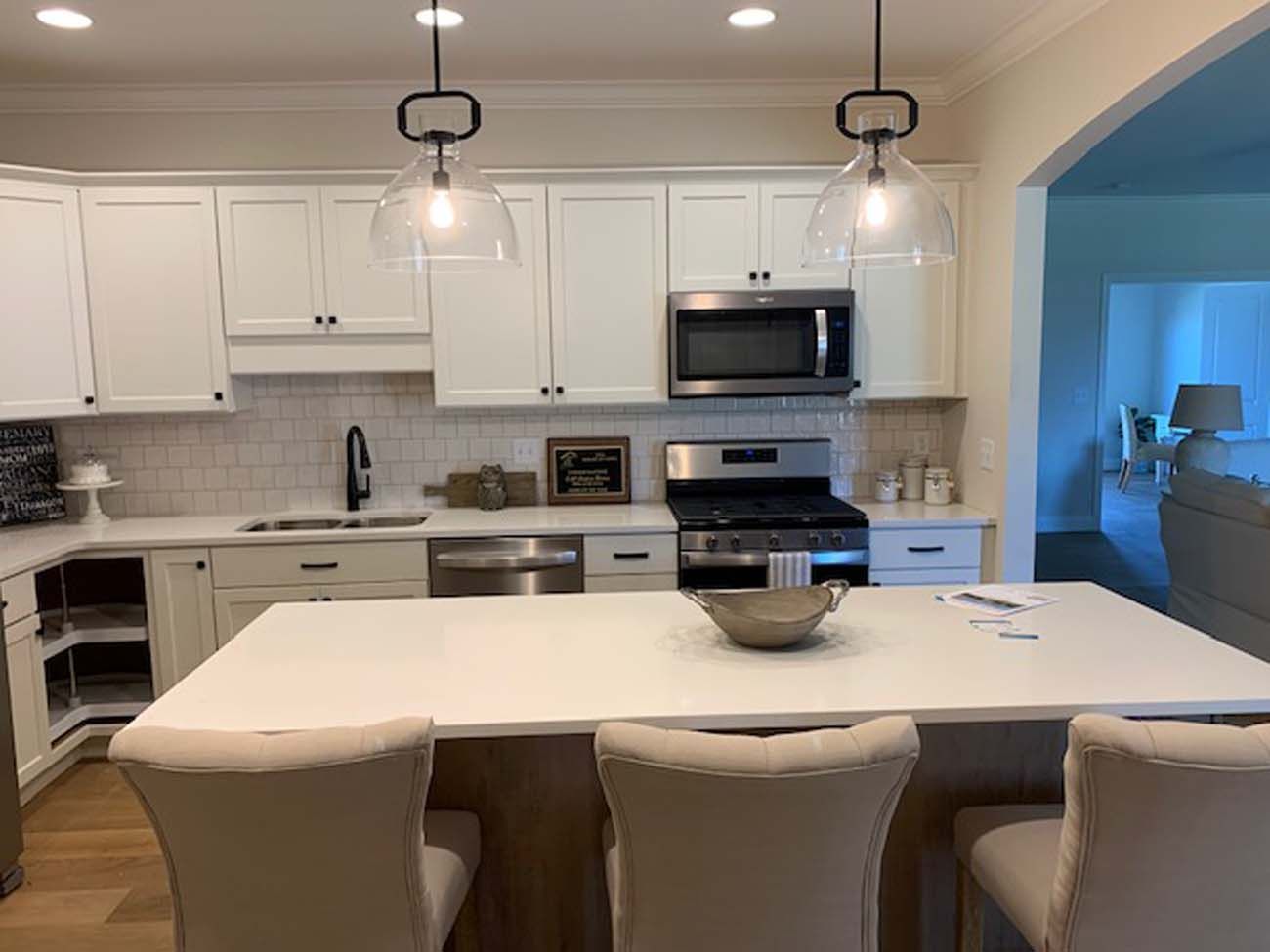 Kitchen with white cabinets, stainless steel appliances, and a light-colored island with three bar stools.