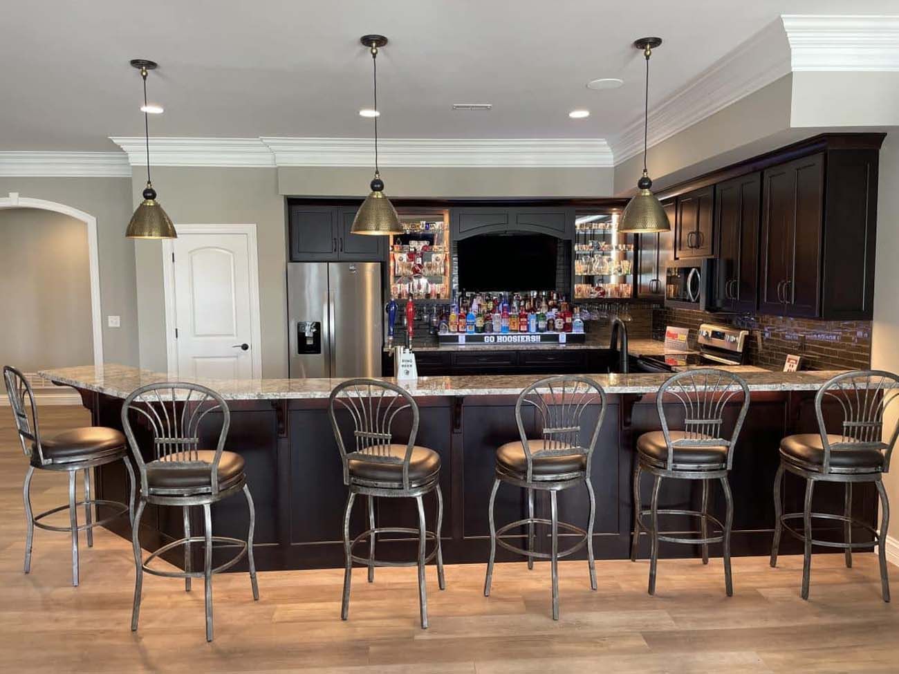 A home bar with granite countertop, dark cabinets, pendant lights, and metal bar stools.