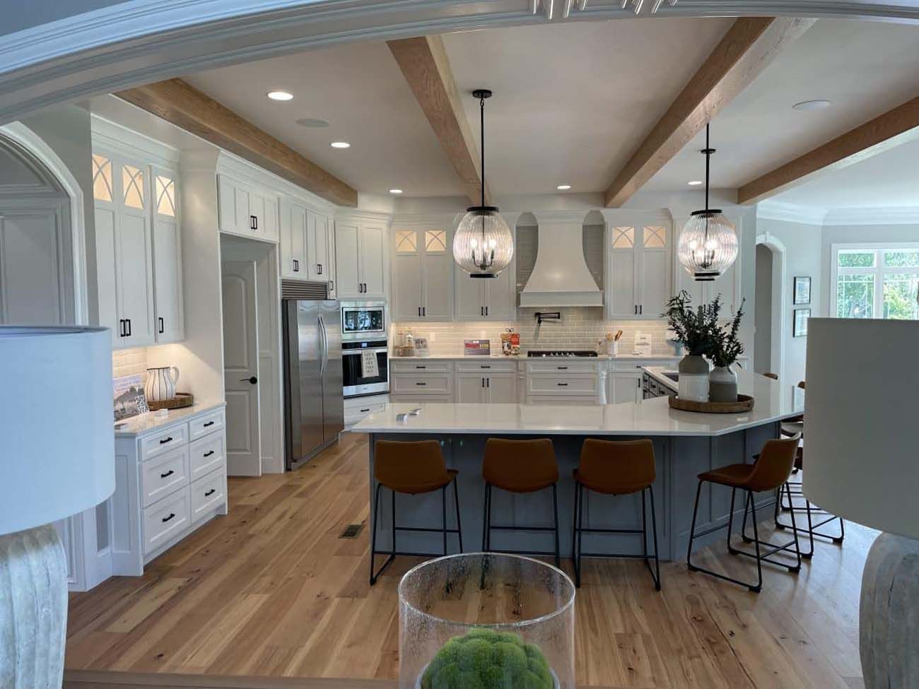 Modern kitchen with white cabinets, wood beams, a gray island, and brown bar stools.