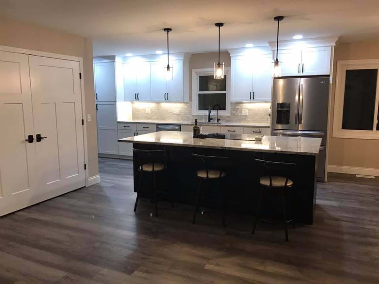 Modern kitchen with a black island, white cabinets, stainless steel appliances, and dark flooring.