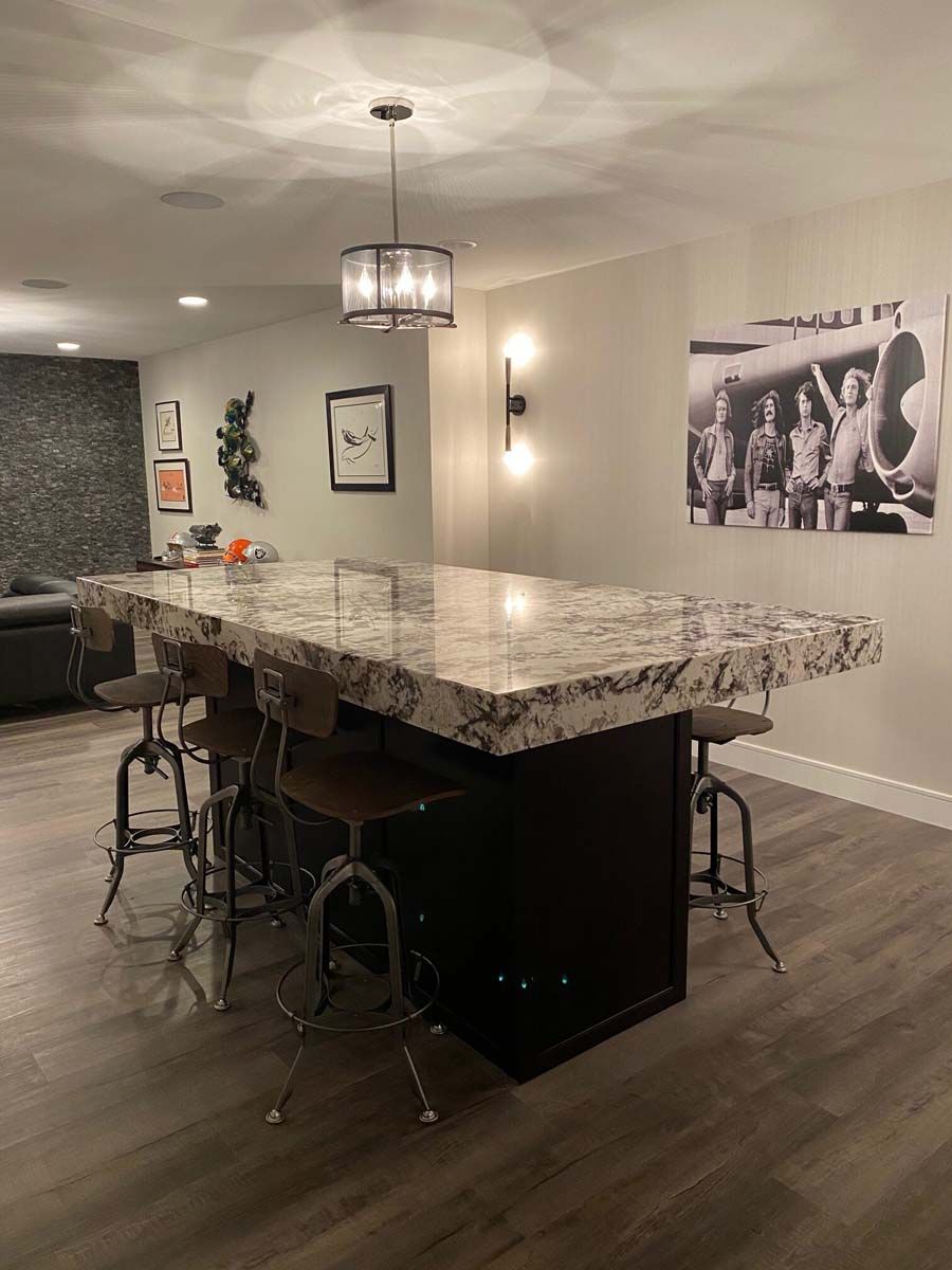 Kitchen island with granite countertop, dark cabinetry, and metal stools. Overhead lighting, photo on wall.
