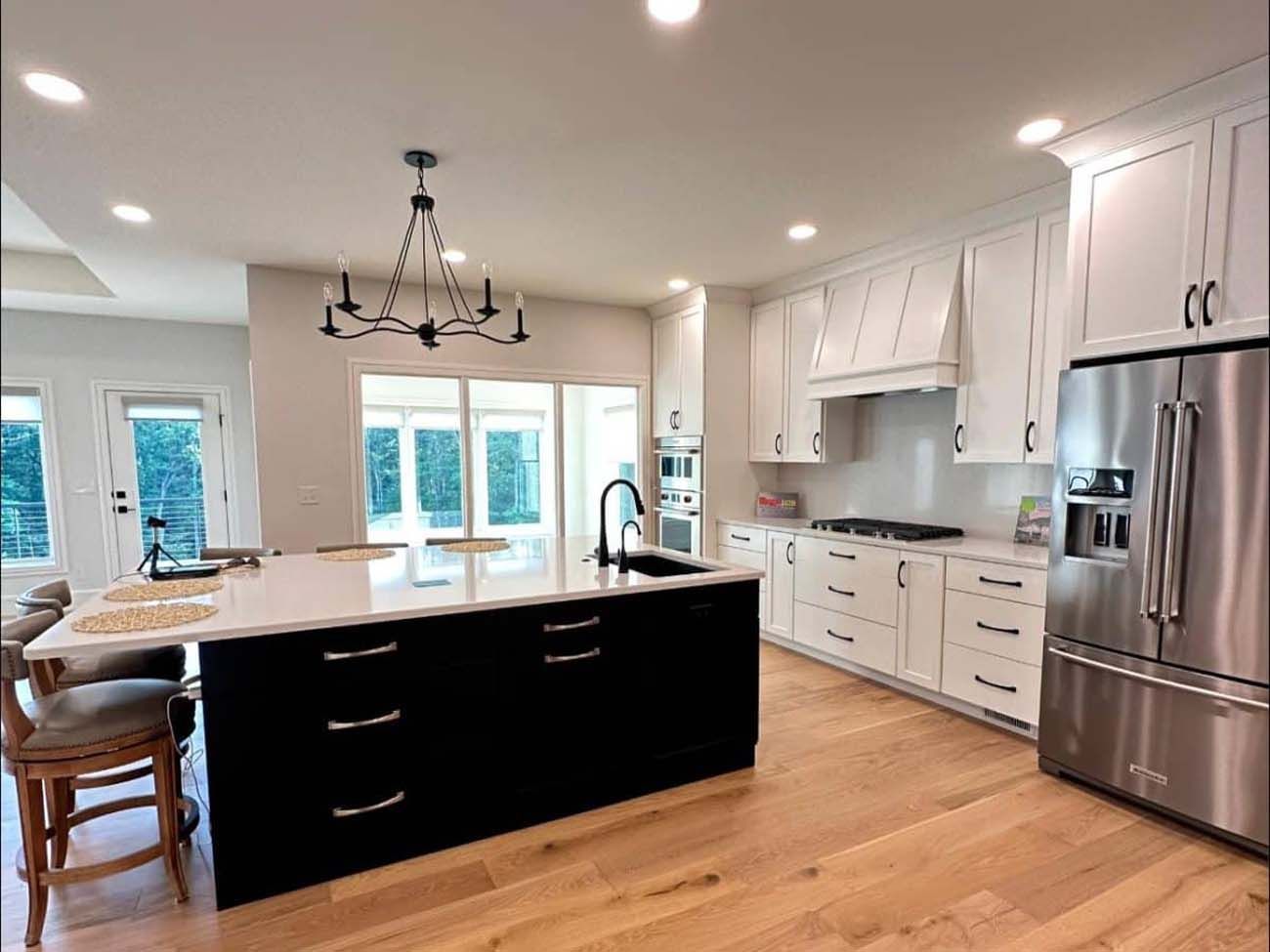 Modern kitchen with white cabinets, black island, stainless steel refrigerator, and wood floor.