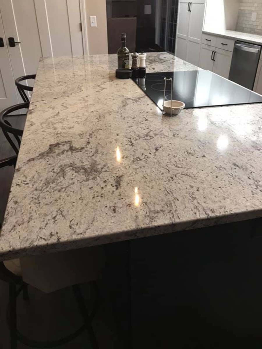 Granite countertop with built-in stovetop. Beige and gray speckled pattern, dark cabinets and black bar stools.