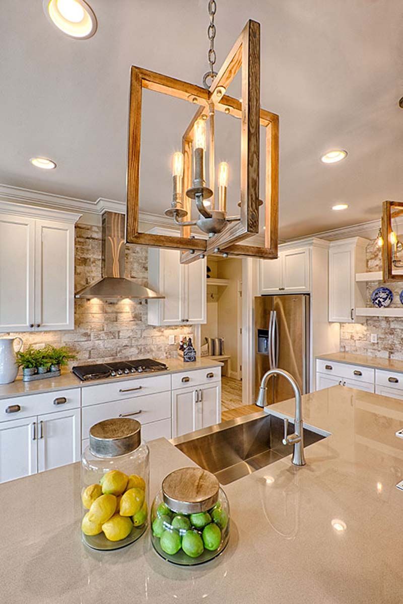 Kitchen with white cabinets, stone backsplash, island with sink, and wooden chandelier.