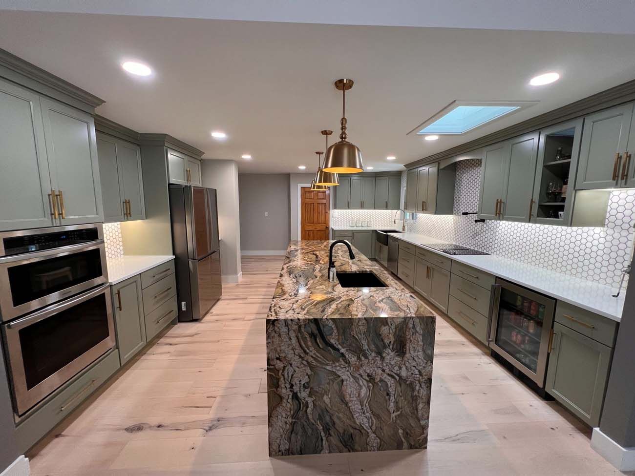 Spacious kitchen with sage green cabinets, light wood floor, and a marble island with gold fixtures.