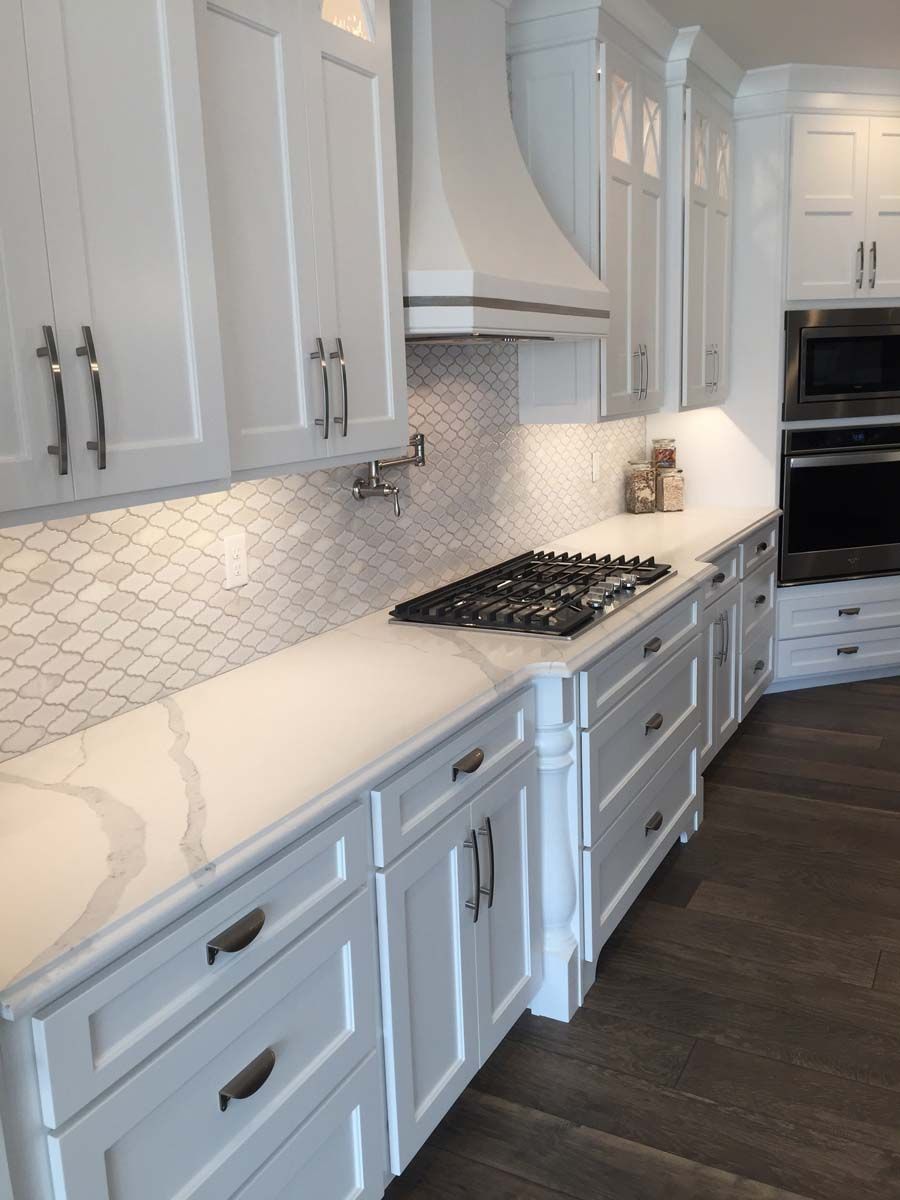 White kitchen with marble countertops, mosaic tile backsplash, and stainless steel hardware.