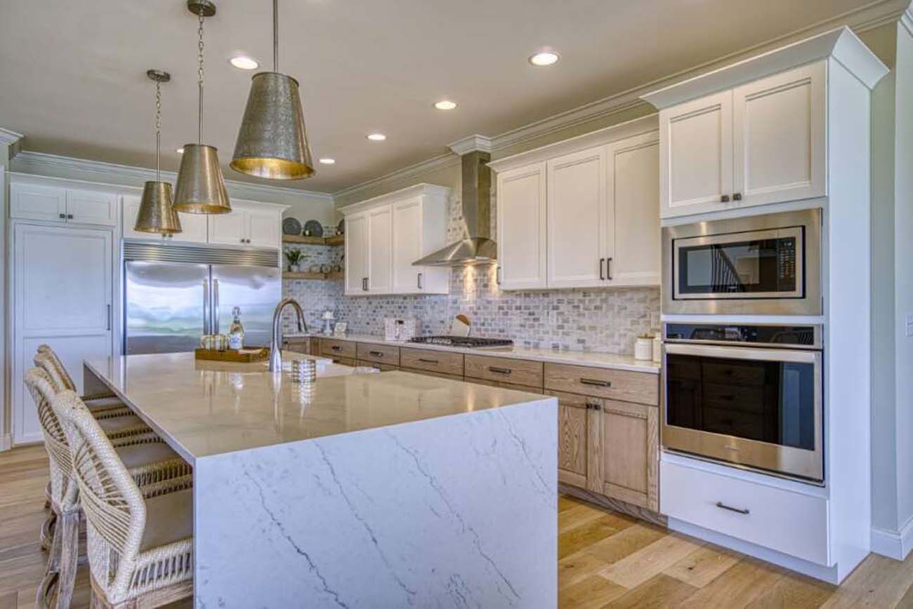Modern kitchen with large island, stainless steel appliances, white and wood cabinets, pendant lights.
