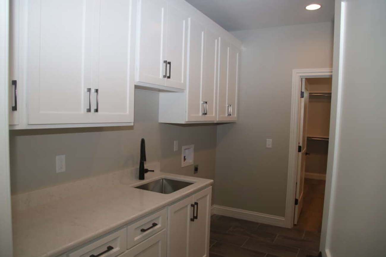 White laundry room with cabinets, sink, and doorway to closet.