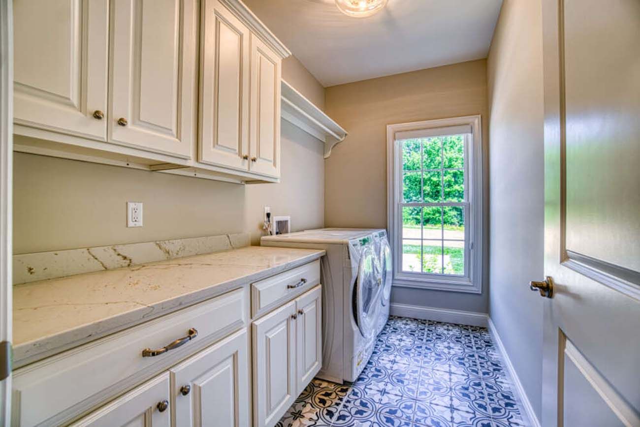 Laundry room with white cabinets, countertop, and washer/dryer. Window shows outside view; patterned floor.