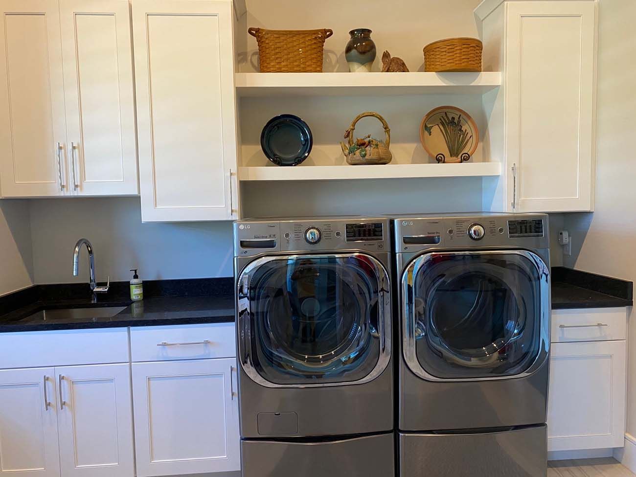 Laundry room with washer, dryer, sink, cabinets, shelves with decorations.