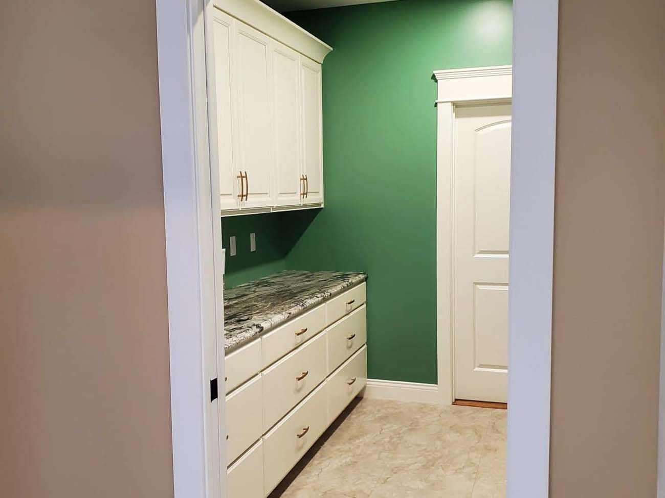 View of a pantry with white cabinets, green wall, and closed white door.