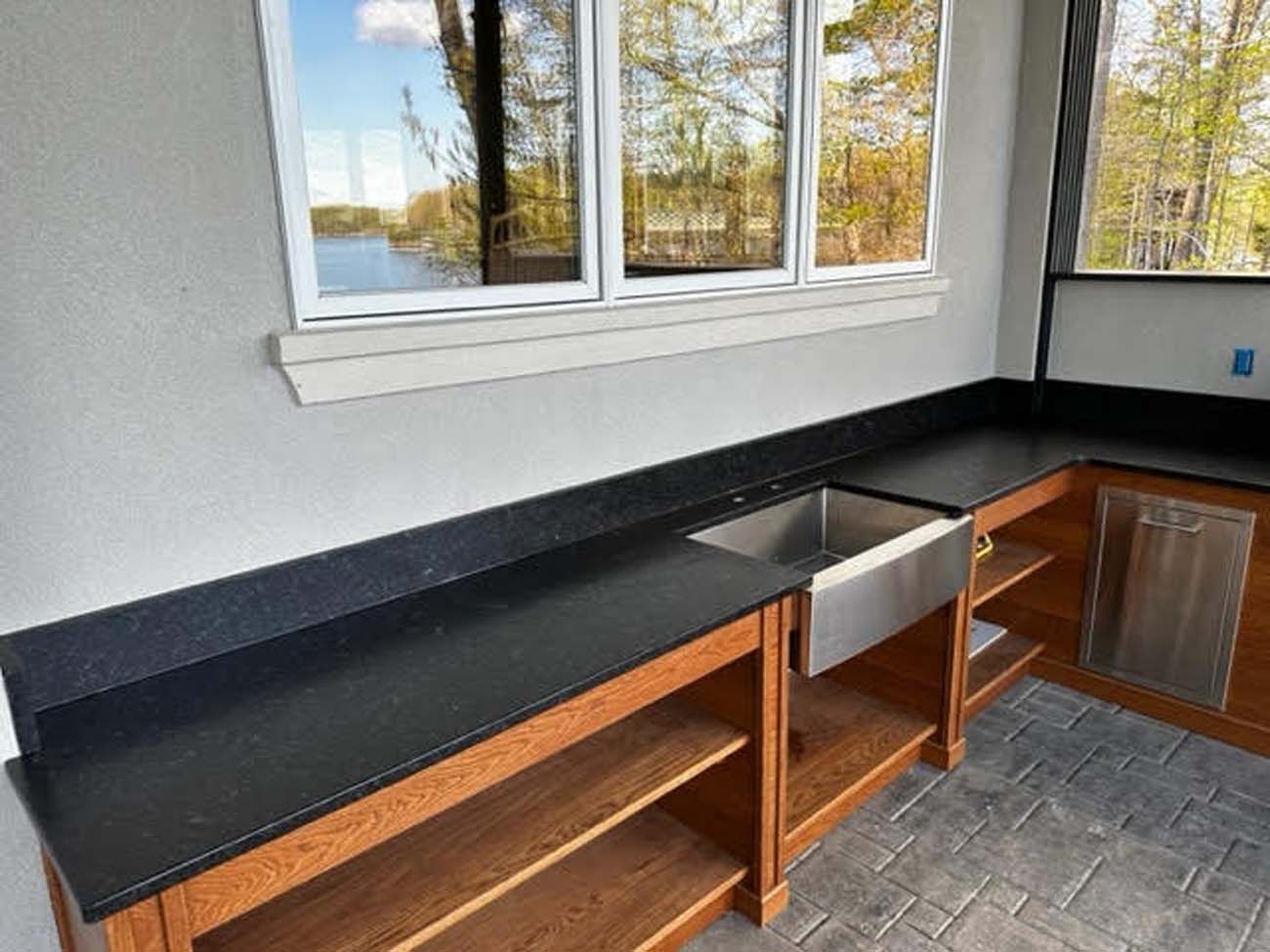 Outdoor kitchen with black countertops, stainless steel sink, and wooden cabinets.