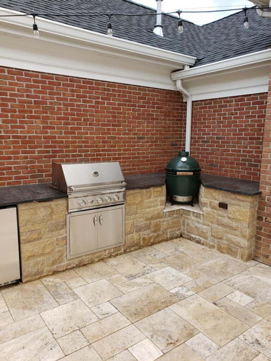Outdoor kitchen with a grill, Big Green Egg, brick wall, and stone countertops.