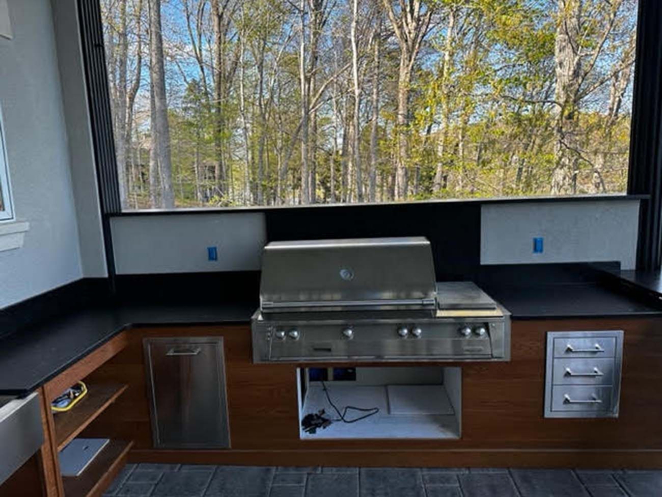 Outdoor kitchen with stainless steel grill, black countertops, and wooden cabinetry.