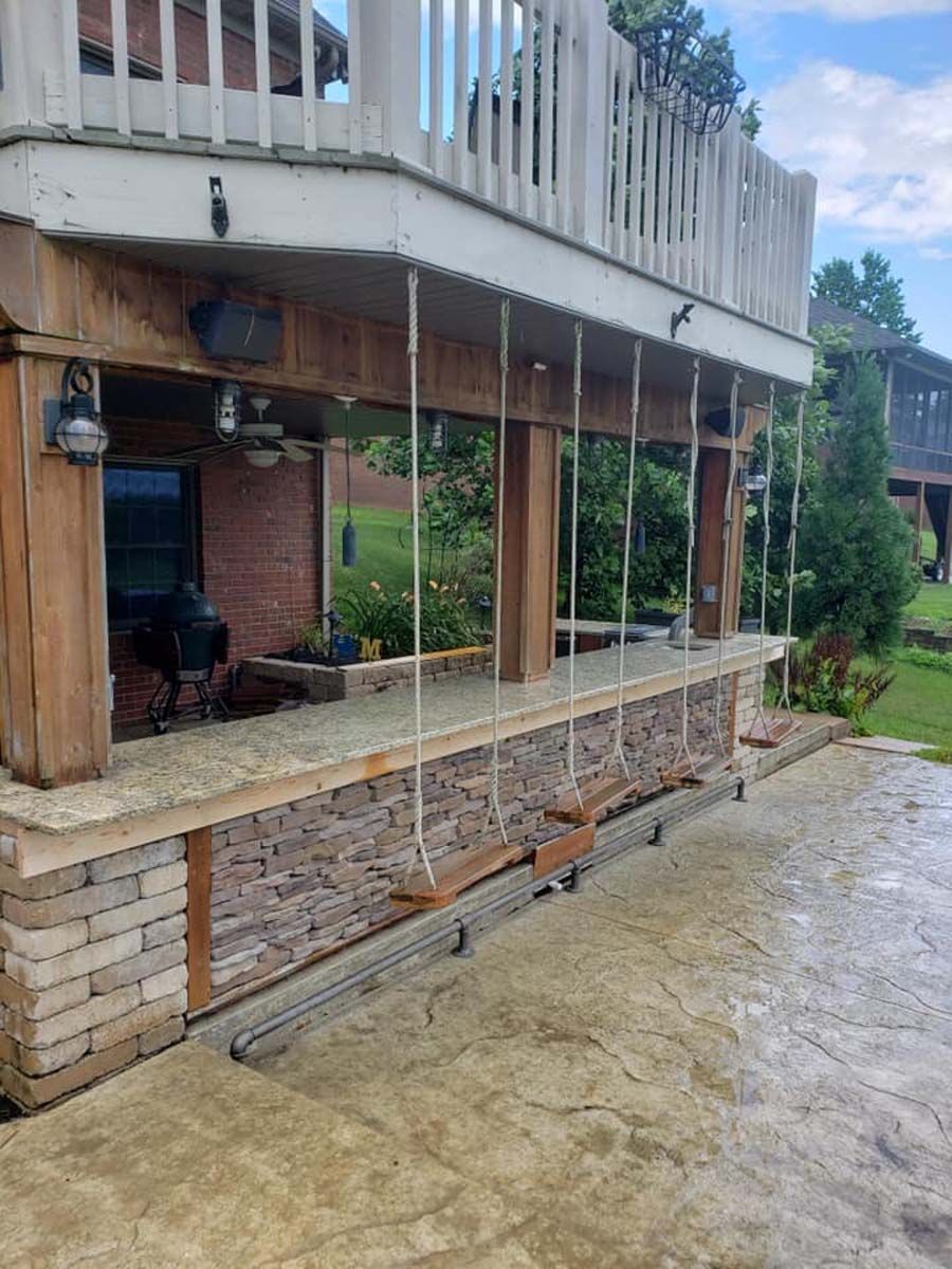 Outdoor bar with stone facade, swings, and upper deck. Brick and wood details, overcast sky.