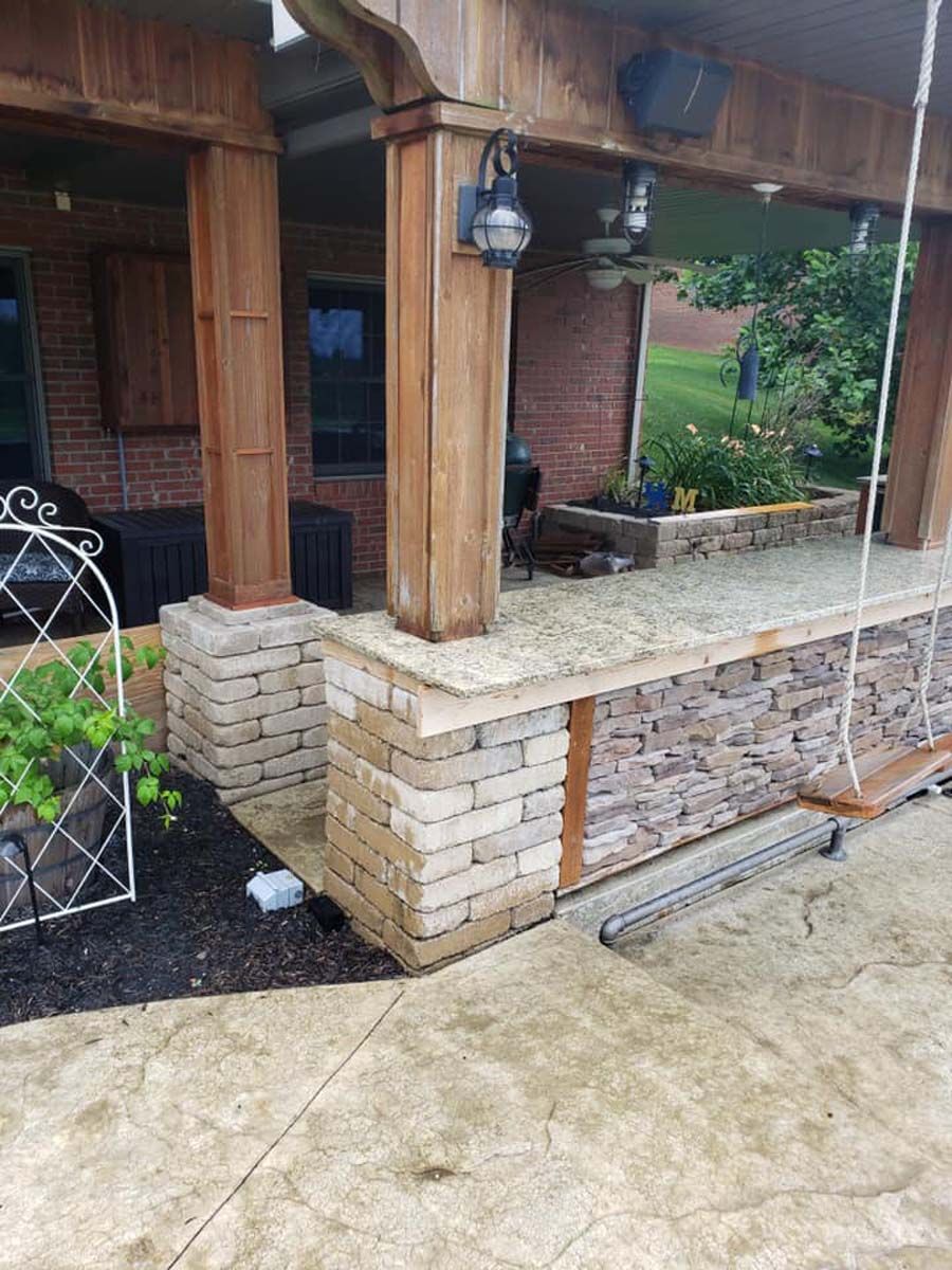 Covered patio with stacked stone and wood pillars, swing, and outdoor speakers.