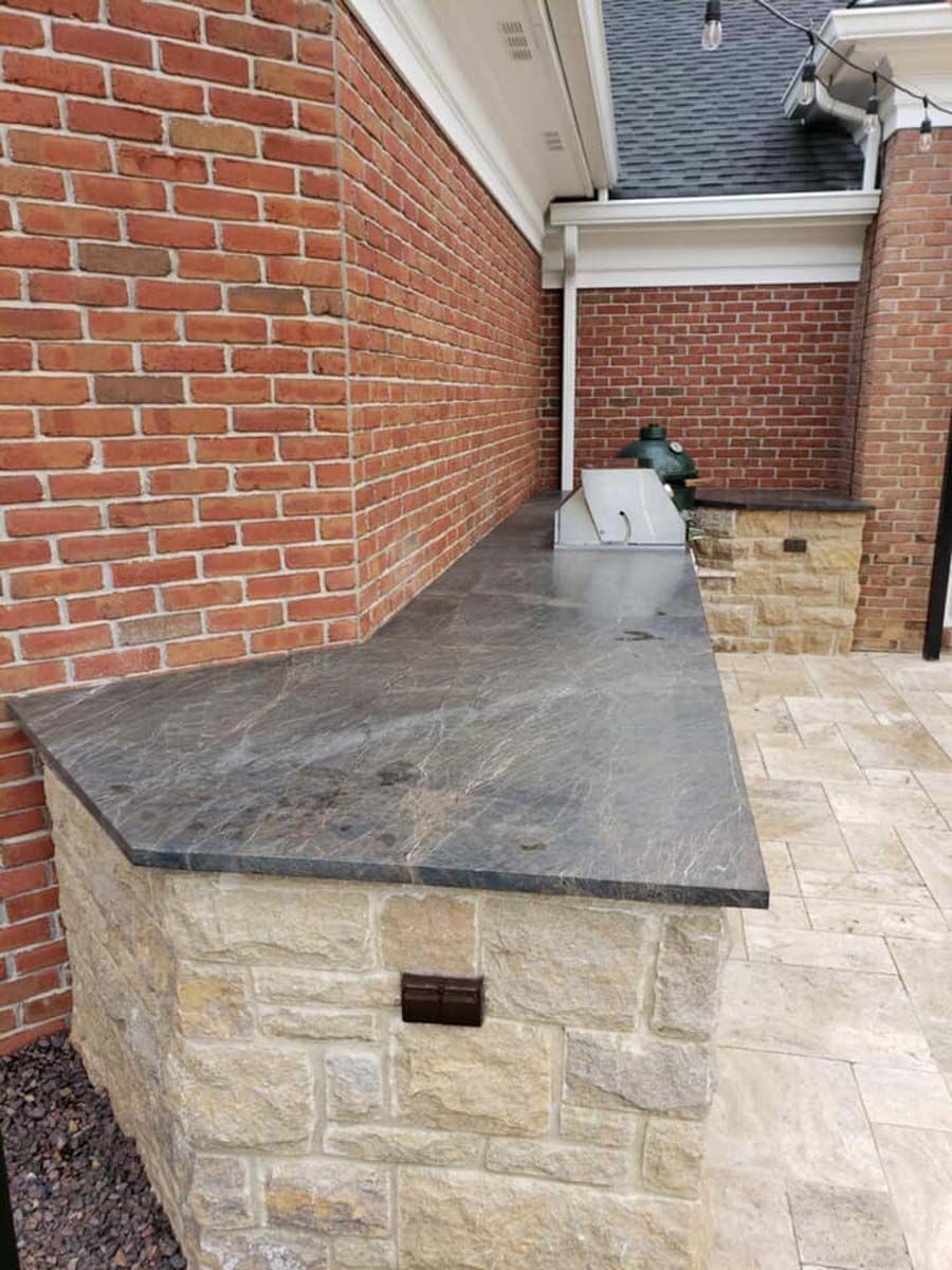 Outdoor kitchen with gray countertop and brick and stone siding.