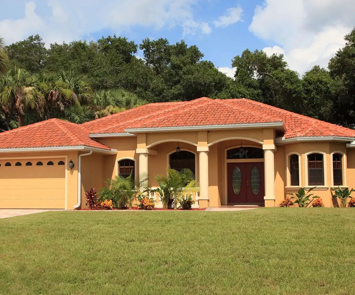 Yellow stucco house with red tile roof, arched entryway, and green lawn.