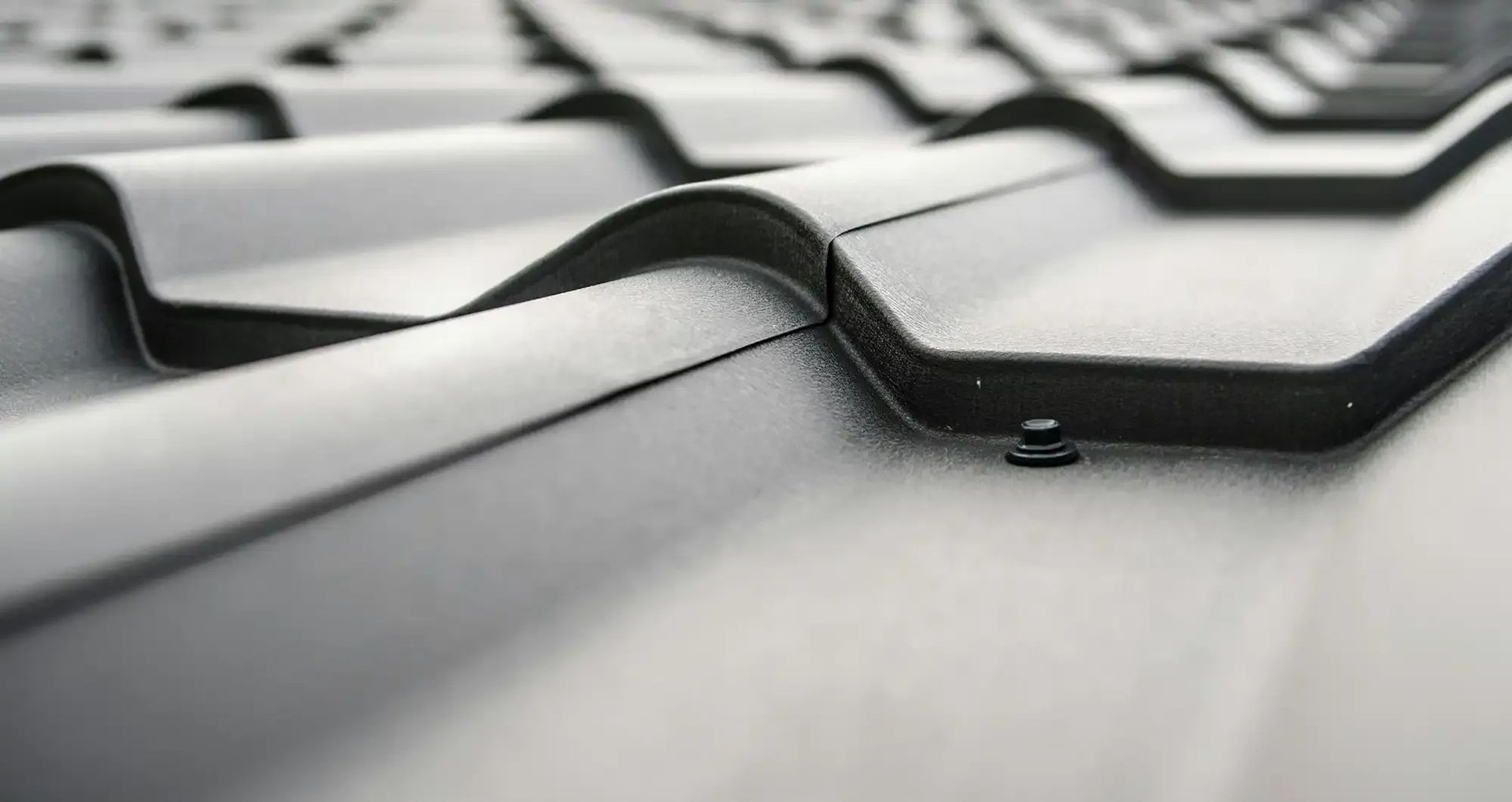Close-up of a dark gray metal roof with a repeating wave-like pattern, angled from the bottom left.